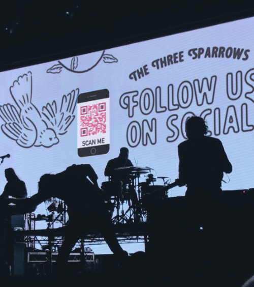 Scenario del palco di un concerto con un QR Code che mostra i canali social della band.