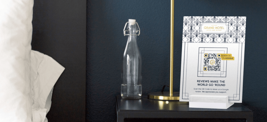 Un comodino in una camera d'albergo con una bottiglia d'acqua, una lampada e un espositore da tavolo con un codice QR.